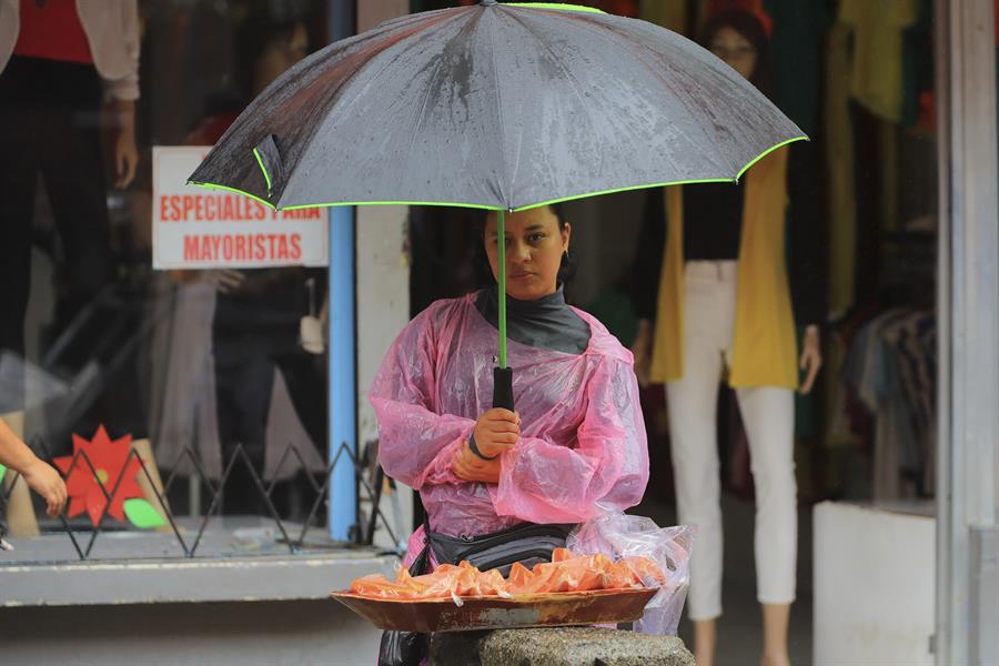Una mujer se protege de la lluvia mientras vende frutas, este lunes en Tegucigalpa (Honduras). /EFE